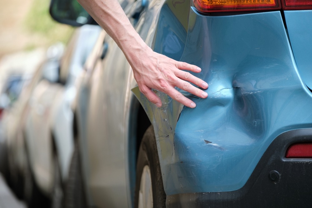 Driver examining a dented car with a damaged fender wonders what to do after a hit and run in NC