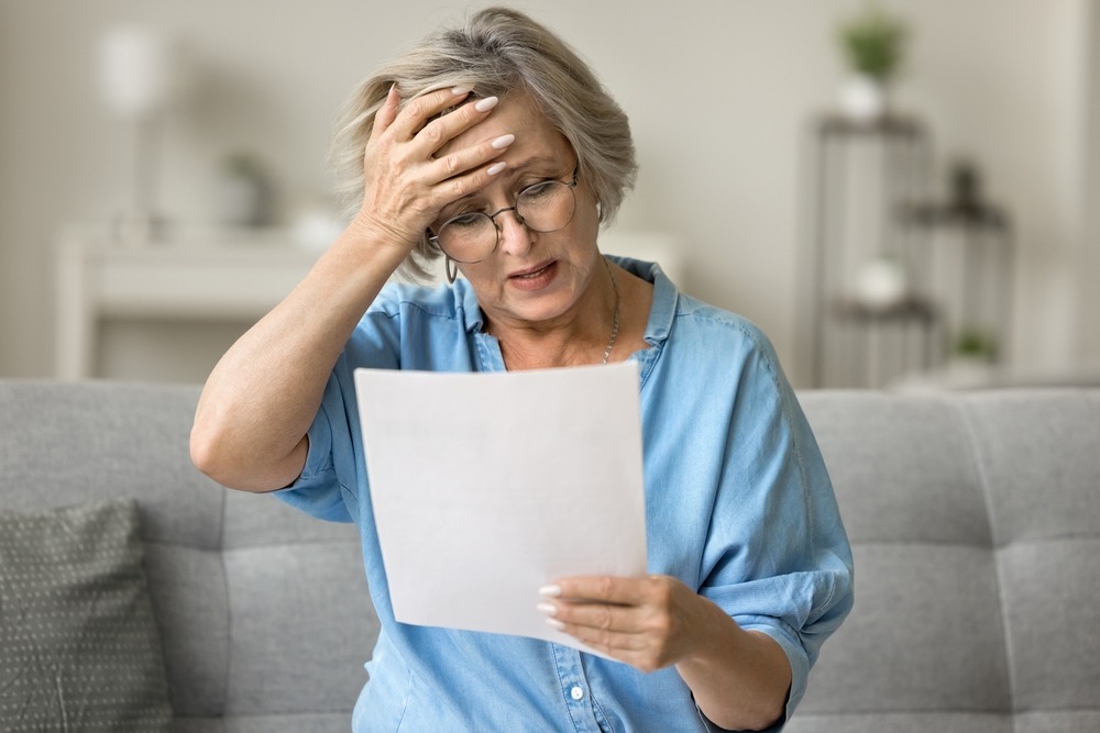 A mature woman is frustratedly looking at a sheet of paper containing medical bills, wondering how medical bills are paid after a car accident in NC.