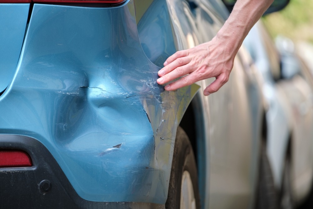 A driver’s hand examining the damage on a blue car after another driver has hit it, and the driver is wondering: “Someone hit my parked car and left in NC – What do I do?