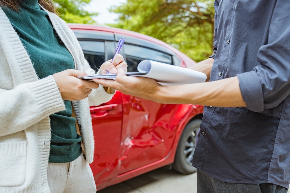 A woman signing a document in front of a crashed car. Can you sue someone for a car accident in NC?