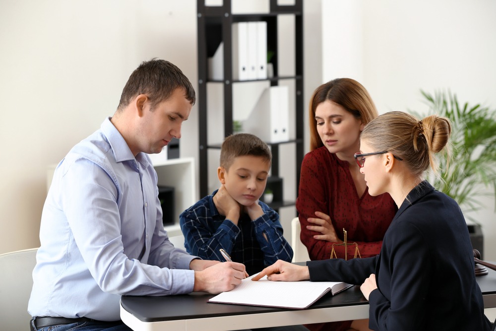 Divorced parents meet with a family lawyer while sitting with their young son during a child custody discussion in an office.